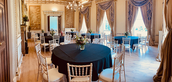 Wedding reception room with round tables, gold chiavari chairs and draped curtains