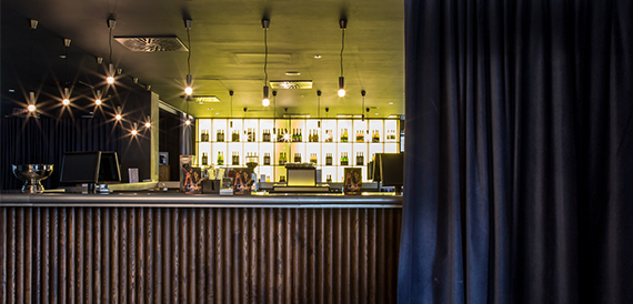Bar counter beneath a wall of illuminated green-lit bottle shelves