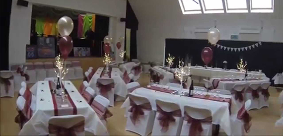 Hall set with burgundy sashes, lit branch centrepieces and bunting