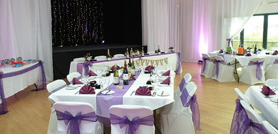 Hall dressed with purple sashes, fairy-light backdrop and bunting on the top table