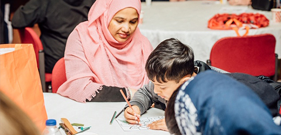 Child drawing at a table with support from an adult helper