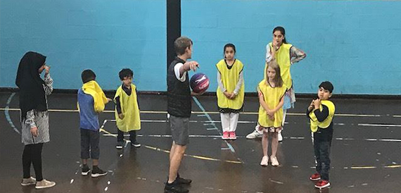 Children playing basketball wearing yellow bibs in the sports hall