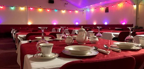 Table laid with fine china tea service beneath coloured string lights