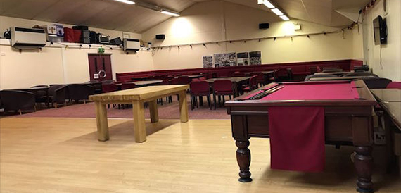 Hall with red-felt pool tables and wooden benches on a wood floor