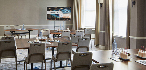 Meeting room set classroom-style with a welcome screen and refreshments