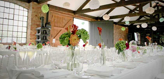 Long dining table set beneath paper pompoms in a brick-walled space