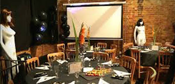 Table set with an orange floral centrepiece before a screen and balloons