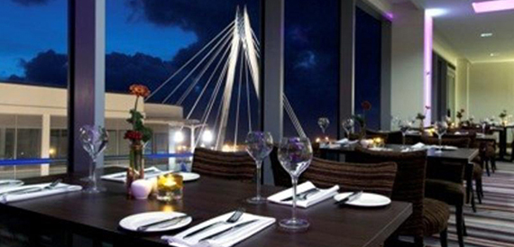 Restaurant tables set for dinner with a lit suspension bridge in view