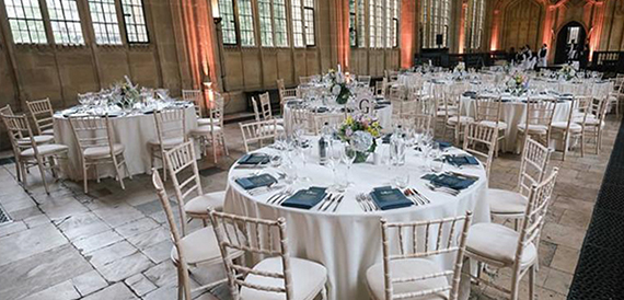 Round tables set formally in a grand stone hall with tall windows