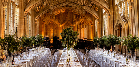 Candlelit dinner table set along a gothic library aisle with stone columns
