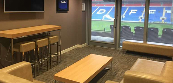 Private box lounge with tan sofas overlooking the pitch