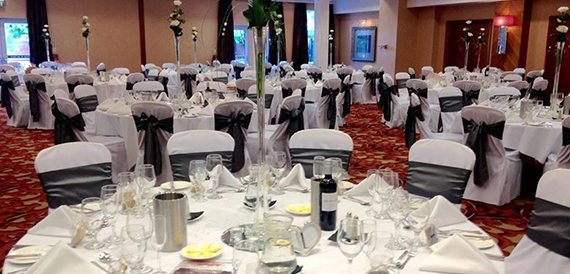 Wedding reception with tall floral centrepieces and black chair sashes on round tables