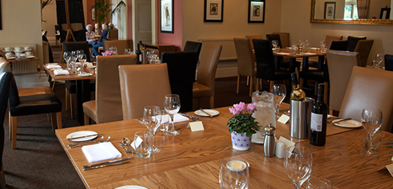 Hotel restaurant with wooden tables set for dinner and tan leather chairs