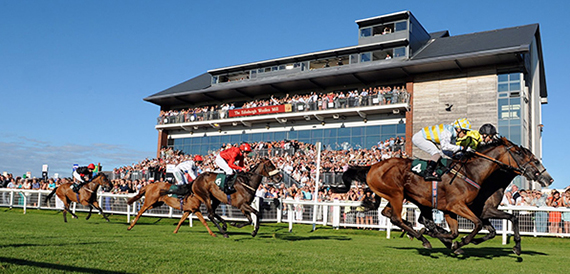 Horses racing past a packed grandstand at Carlisle Racecourse