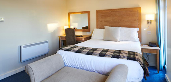 Hotel bedroom with a wood headboard, white linens and a plaid throw