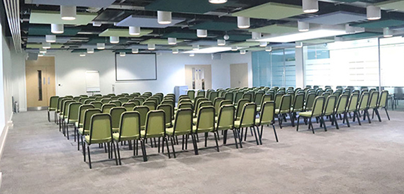 Meeting room set theatre-style with green chairs facing a projector screen