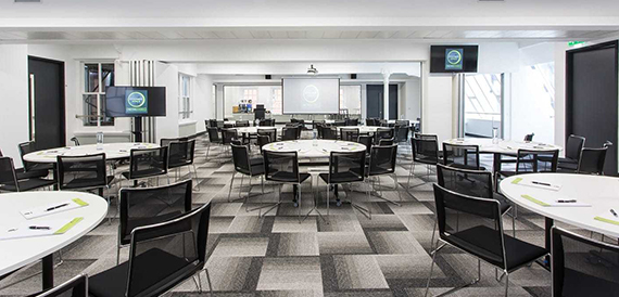 Round tables set cabaret-style with black chairs on chequered flooring