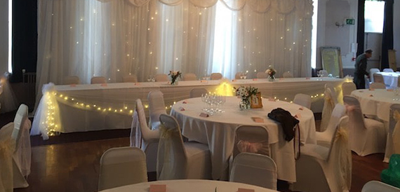 Table set against a fairy-lit curtain backdrop with white chair covers