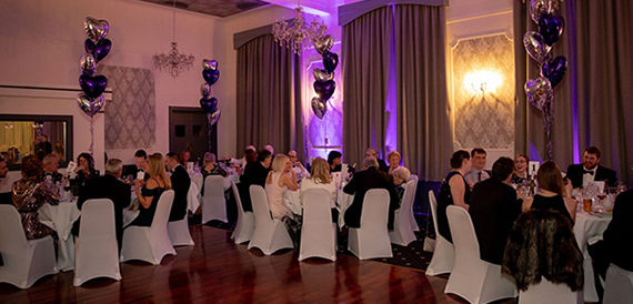 Guests seated at round tables in evening wear with heart balloons