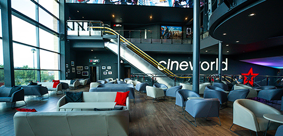Cinema lobby lounge with grey sofas beside an escalator and Cineworld signage