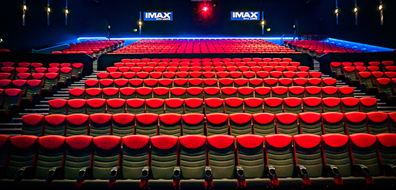 Wide view of an IMAX auditorium with red seating beneath two IMAX signs
