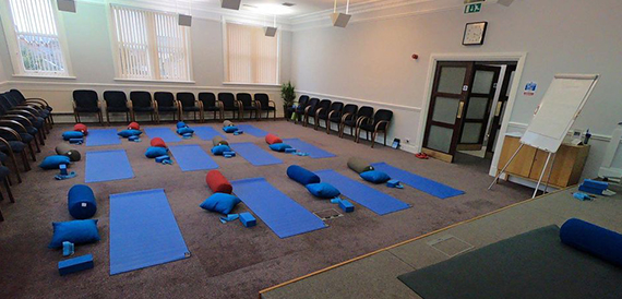 Yoga mats and bolsters laid out in a room with chairs along the wall