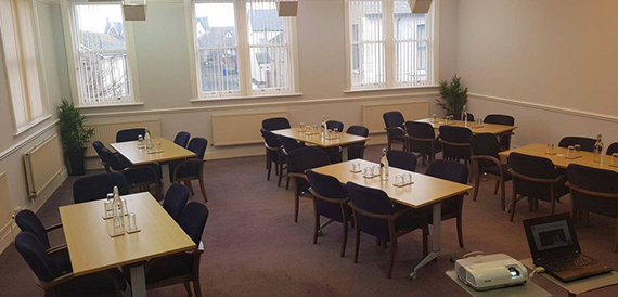 Meeting room set with several small tables, navy chairs and a projector