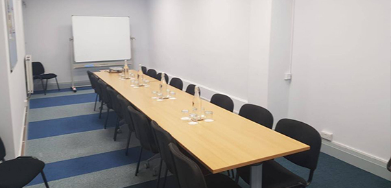 Long boardroom table with black chairs facing a whiteboard