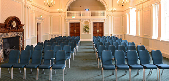Grand hall set theatre-style with blue chairs beneath a gilded arched ceiling