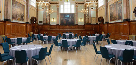 Grand hall set with round tables in white linen and teal chairs facing the stage