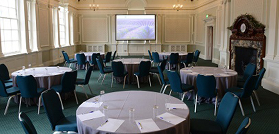Round tables set cabaret-style with teal chairs and a lavender presentation screen