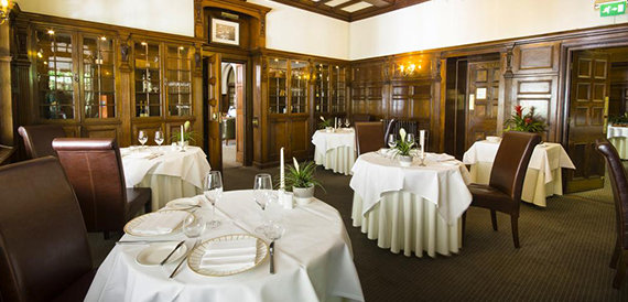 Wood-panelled restaurant with round tables in white linen and leather chairs