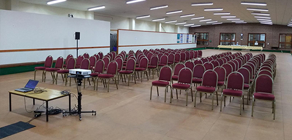 Hall set theatre-style with rows of red chairs and a projector