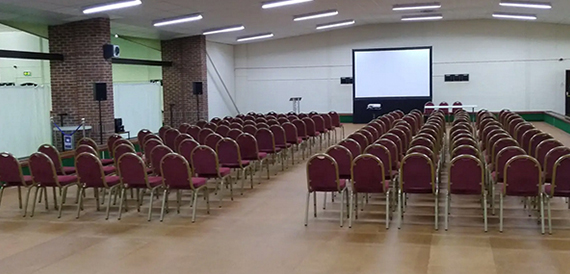Hall set theatre-style with rows of red chairs facing a screen