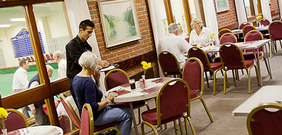 Cafe area with red chairs where a waiter serves seated members