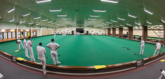 Wide view of an indoor bowls green with players in white kit