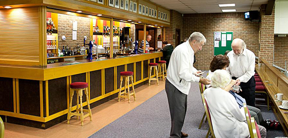Wood-panelled bar counter where staff serve chatting members