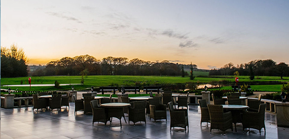 Outdoor terrace with rattan seating overlooking green fields at sunset
