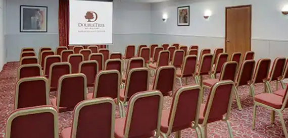 Theatre-style meeting room with rows of burgundy chairs facing a branded screen.