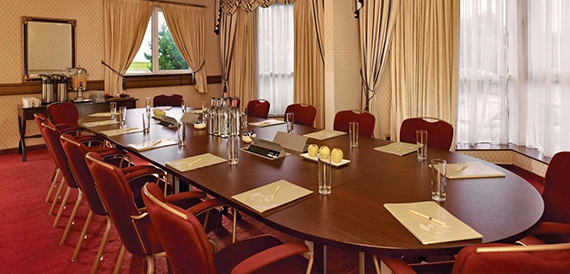 Boardroom with a long dark wood table, burgundy leather chairs and water glasses.