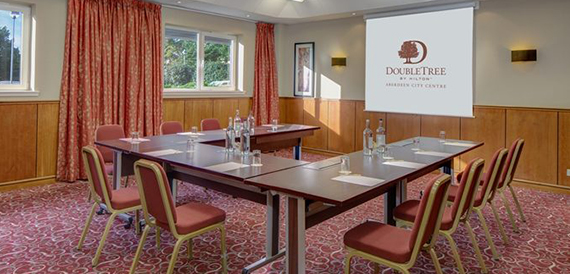Another U-shaped meeting room angle showing burgundy chairs and a branded presentation screen.