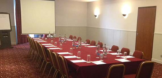Meeting room set boardroom style with a projector screen and a flipchart easel.