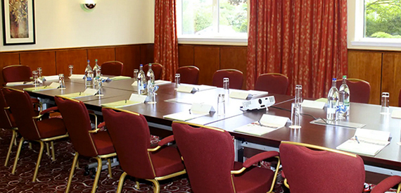 U-shaped boardroom with a projector, red curtains and rows of burgundy chairs.
