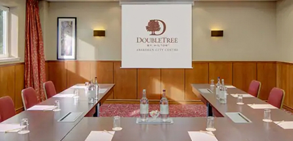 U-shaped meeting room set with water bottles, burgundy chairs and a branded screen.
