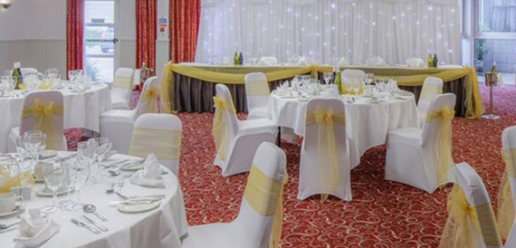 Wedding reception room with round tables, white linen and gold chair sashes.