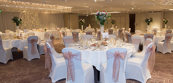 Wedding reception room with round tables dressed in pink chair sashes