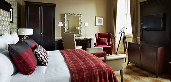 Hotel bedroom with a tartan bedspread and a red armchair