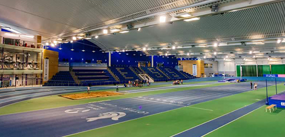 Wide view of an indoor athletics arena with tiered blue seating and a track.