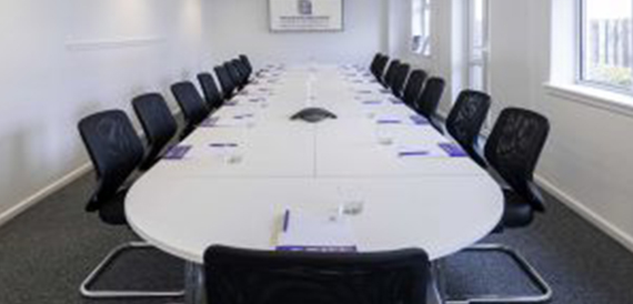Long white oval table with black chairs set for a meeting.