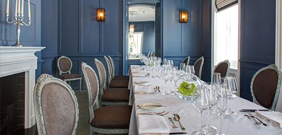Dining room with dark blue walls, a long table and cream upholstered chairs.